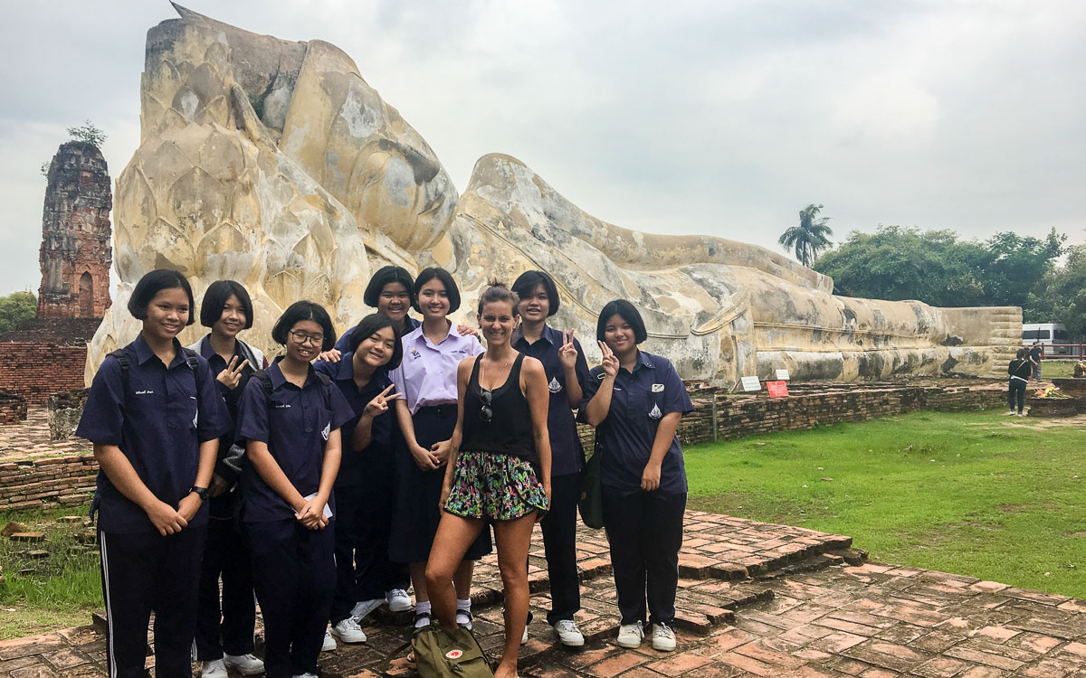 uma mulher ocidental rodeada de meninas tailandezas e um monumento de budha ao fundo