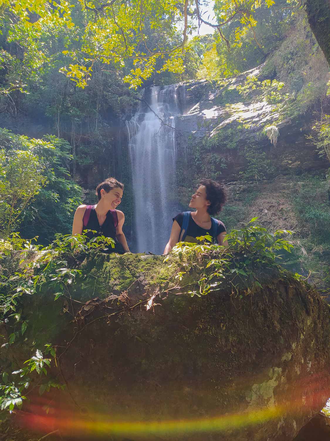 duas mulheres se olhando e uma cachoeira ao fundo